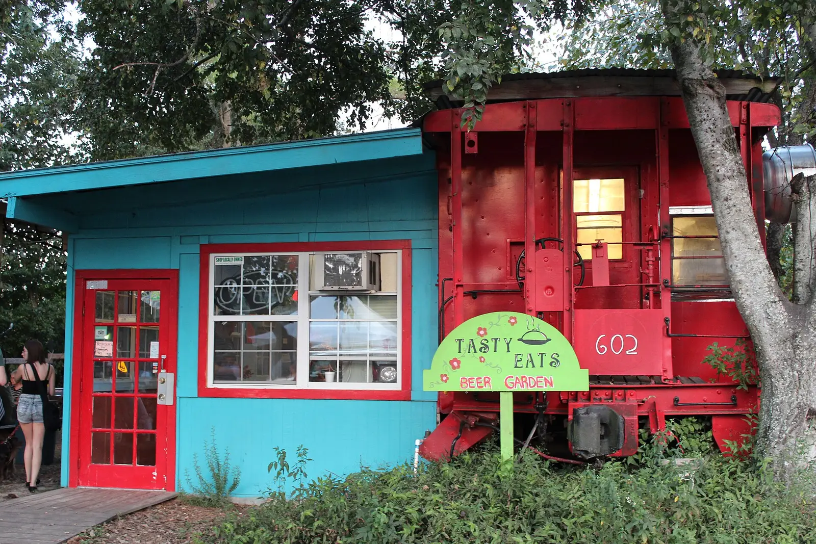 A red caboose beside a teal storefront at the Railroad Square Art District in Tallahassee.